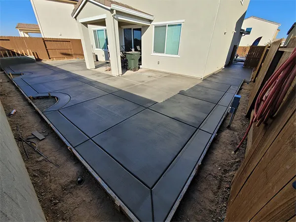 Clean broom-finished concrete slab poured along a backyard fence
