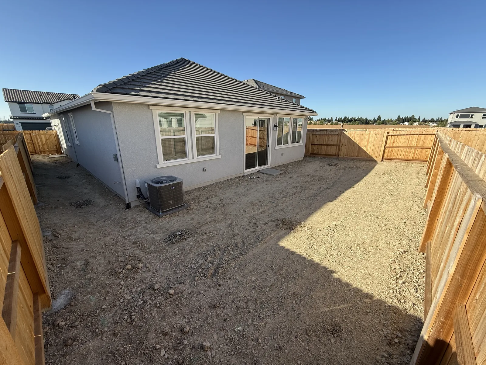 Bare graded-dirt backyard of a newly built single-story home with new wood fences, before any landscaping