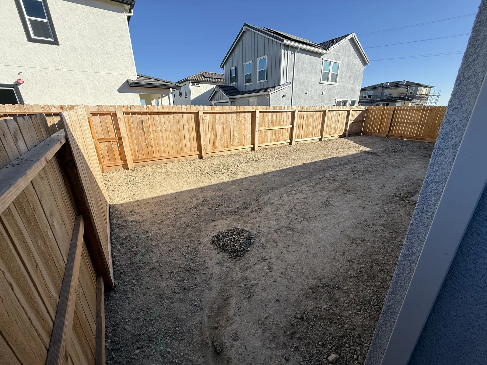 Bare graded-dirt backyard of a newly built home with a wood fence, before landscaping