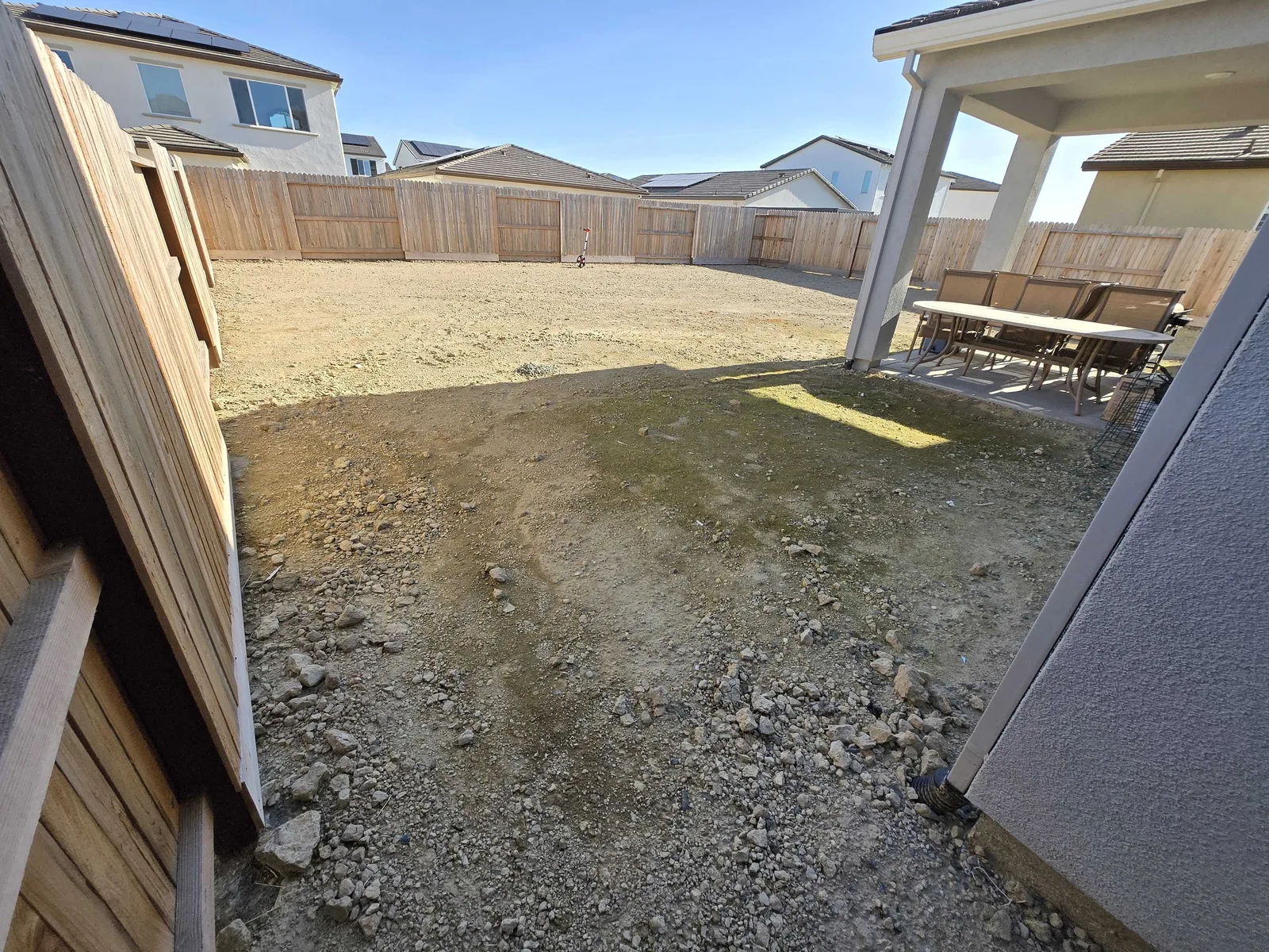 New-build backyard of bare graded dirt beside a small covered patio, before a concrete patio