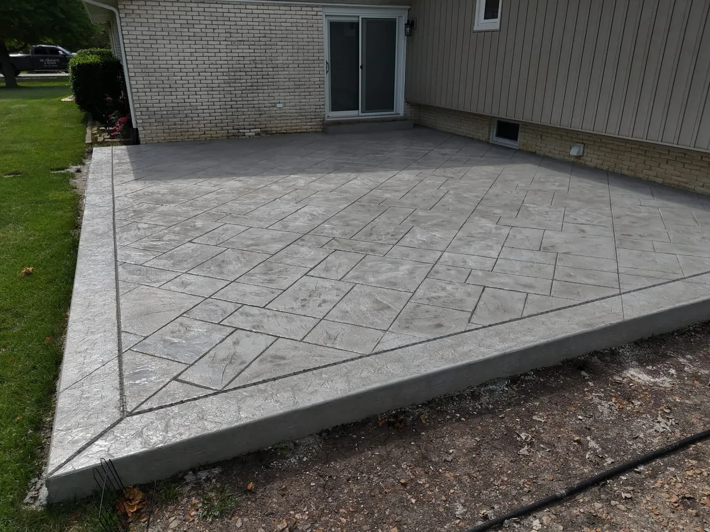 Gray stamped concrete patio in an ashlar slate pattern with a diagonal border band beside a brick house