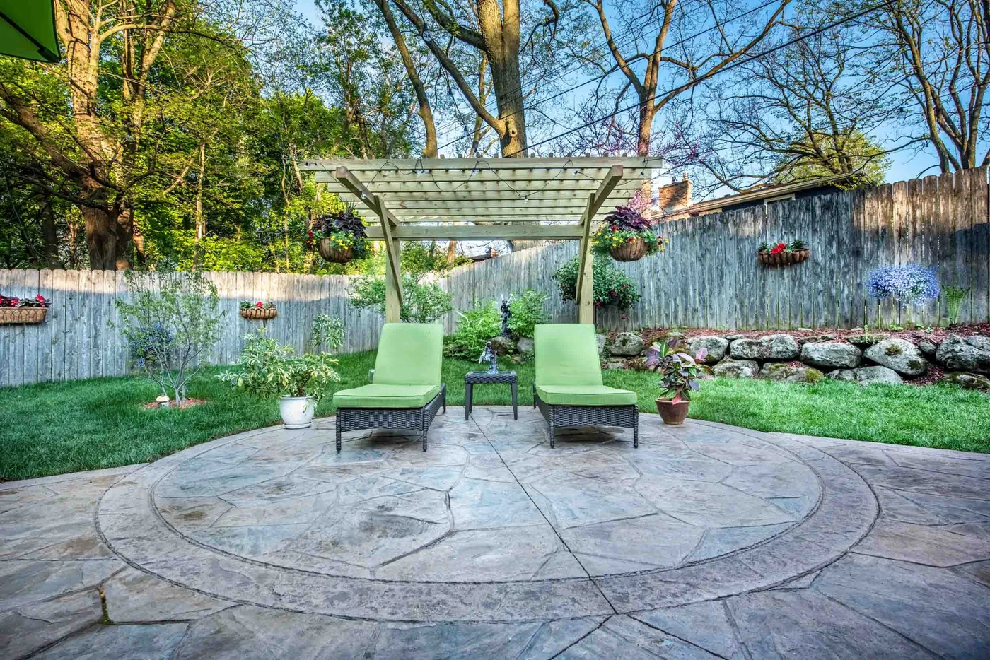 Circular stamped concrete patio in a flagstone pattern under a wood pergola with two lounge chairs