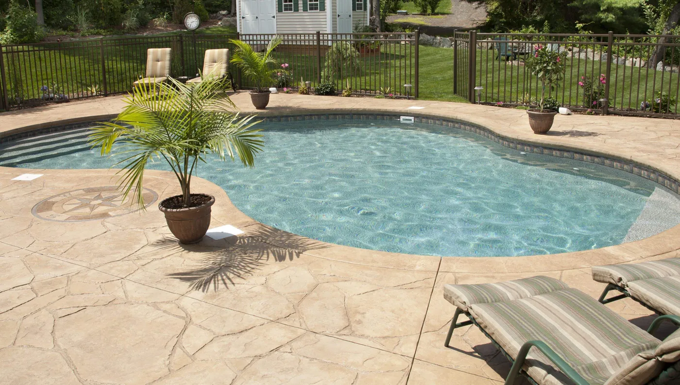 Tan stamped concrete pool deck in a flagstone pattern with a compass medallion beside a curved pool