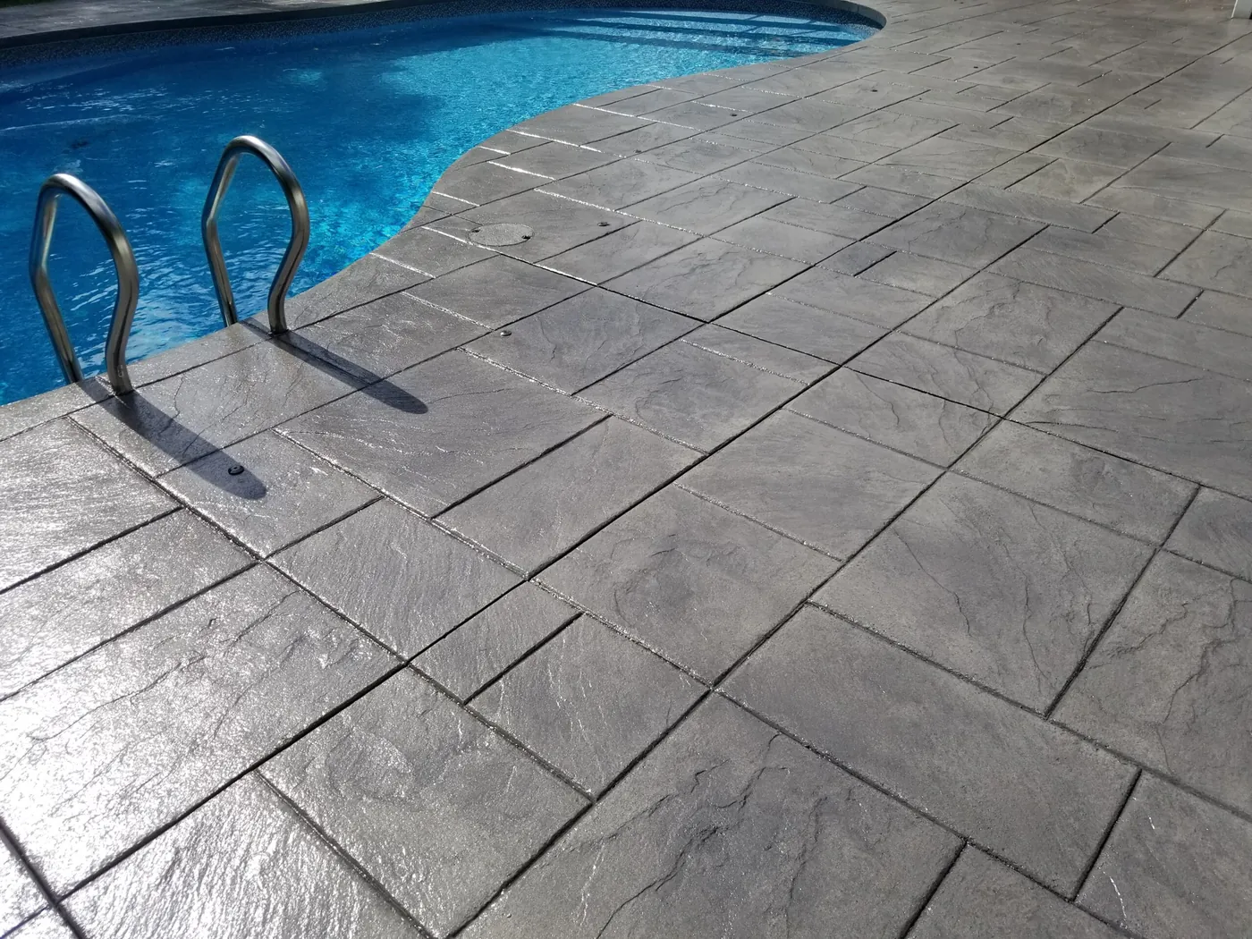 Gray stamped concrete pool deck in an ashlar slate pattern beside a pool ladder